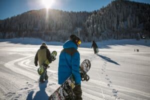 Snowboarders walking through fresh snow towards the slopes, showcasing a sunny winter day in a mountainous landscape, emphasizing Vista Bahn's snowboard rental services.