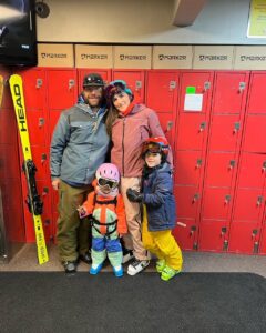 Family of four in ski gear posing in front of red lockers, showcasing Vista Bahn's ski rental service and family-friendly atmosphere.