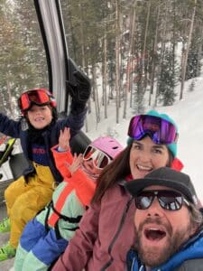 Family enjoying a gondola ride in snowy mountains, smiling and wearing ski gear, highlighting the fun and excitement of a ski trip with Vista Bahn Ski Rentals.