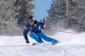 Skier in blue outfit carving through fresh snow on a mountain slope, showcasing the thrill of skiing at Vista Bahn Ski Rentals in Vail, Colorado.